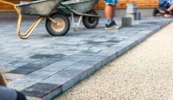 Laying gray concrete paving slabs in house courtyard driveway patio. Professional workers bricklayers are installing new tiles or slabs for driveway, sidewalk or patio on leveled
foundation base made of sand at public or private residence.